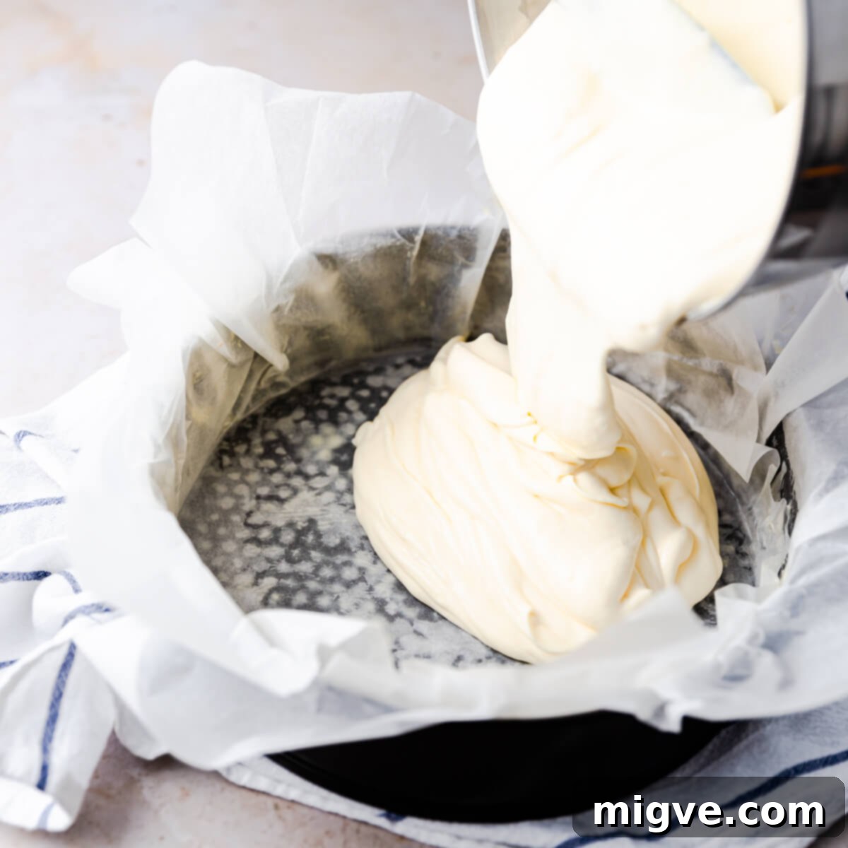 cheesecake batter being poured into baking tin lined with baking paper, showing its smooth consistency.