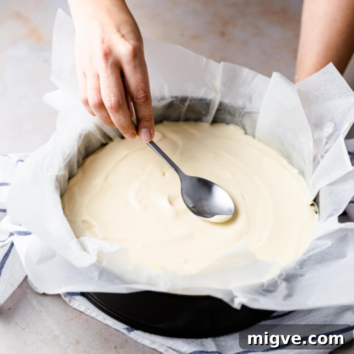 top of the cheesecake batter being smoothed out with the back of a spoon before baking.