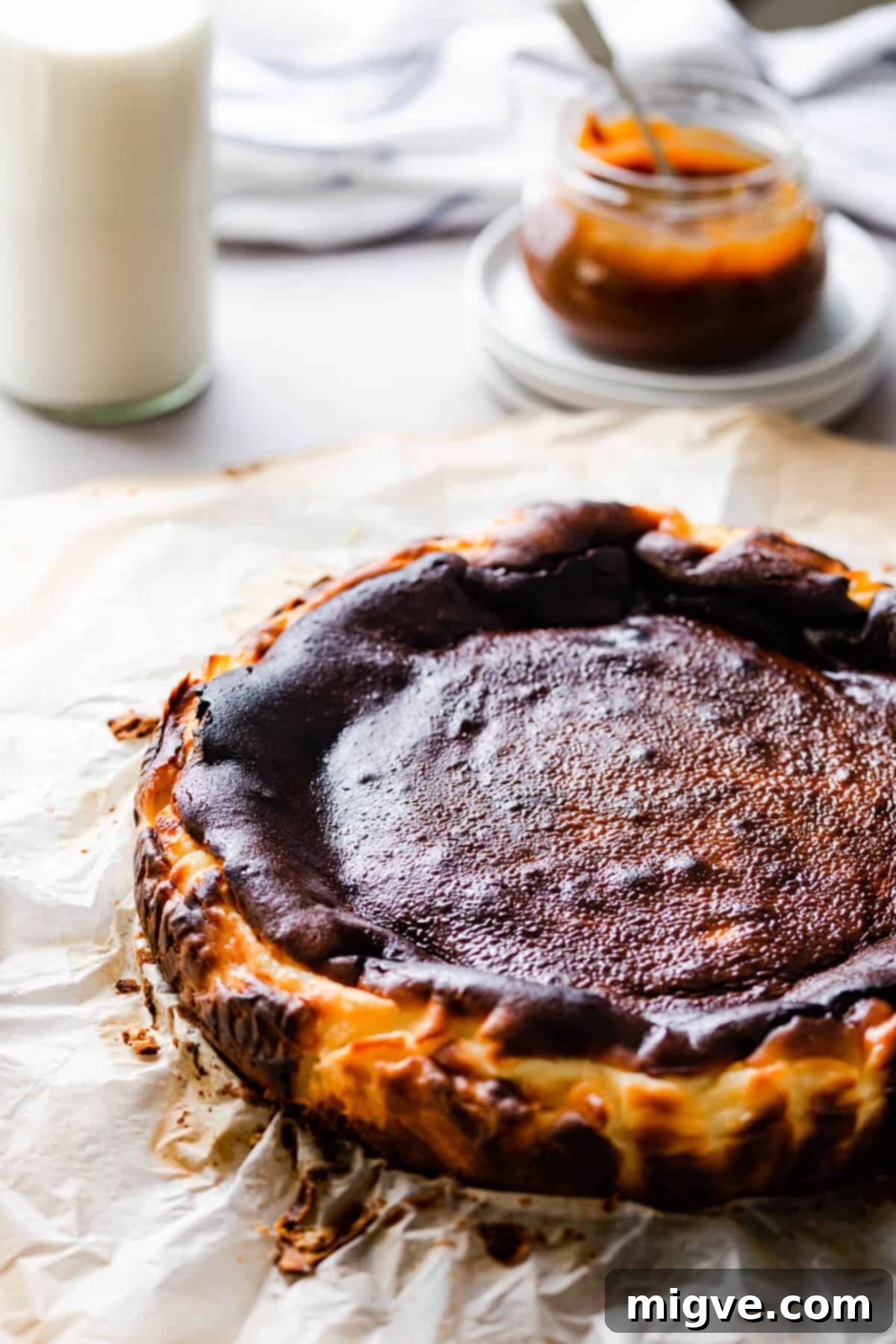 side angle of a beautifully burnt Basque cheesecake resting on some baking paper, highlighting its rustic edges.