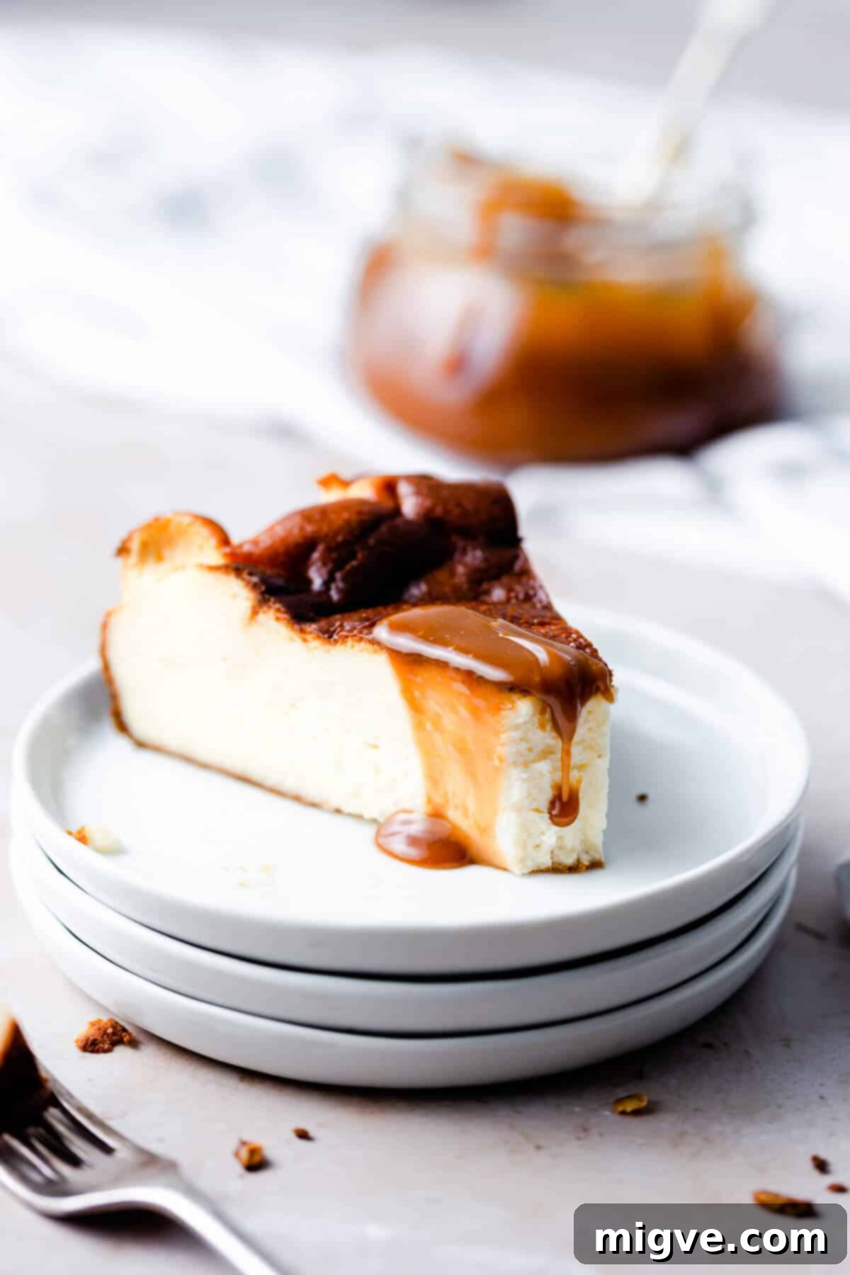 side angle close up at a slice of burnt cheesecake with a bite missing and some caramel sauce dripping from top, highlighting its creamy texture.