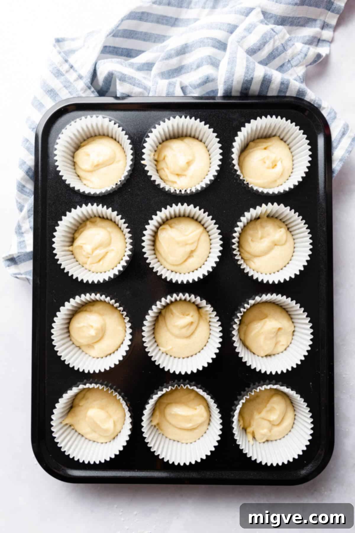A top-down view of a cupcake tray meticulously lined with paper cases, each precisely filled with cupcake batter, ready for baking.