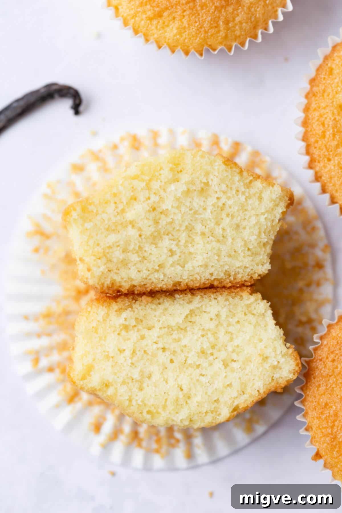 An overhead shot of a freshly baked vanilla cupcake expertly sliced in half, revealing its incredibly fluffy, light, and airy interior texture.