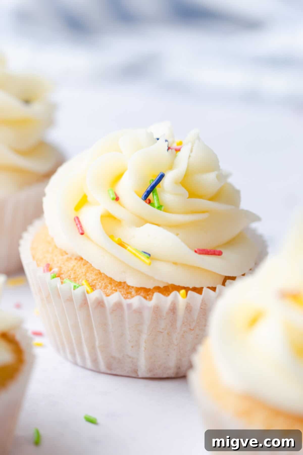 A side close-up of a delightful one-bowl vanilla cupcake, lavishly topped with creamy buttercream and adorned with a scattering of colorful sprinkles.