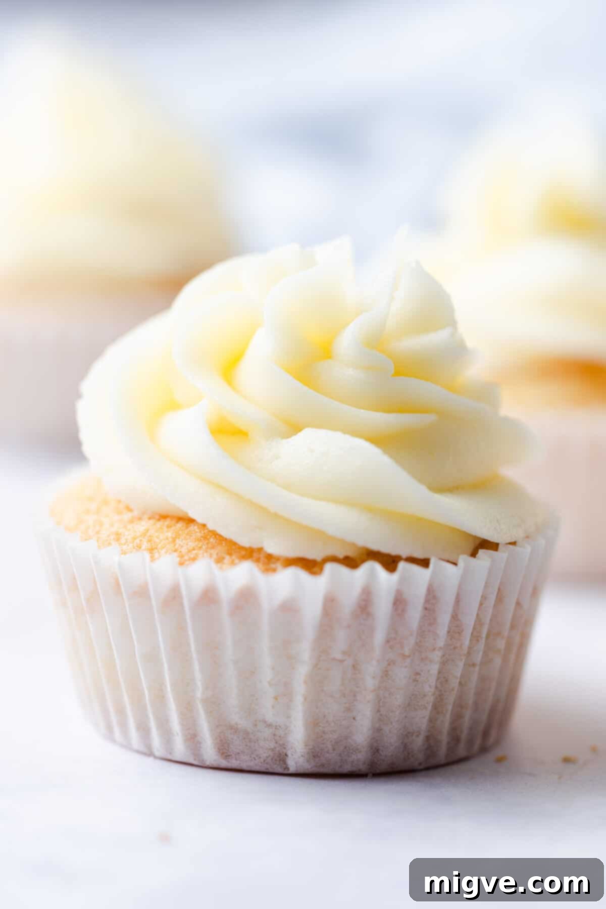 A straight-ahead super close-up of a perfectly baked vanilla cupcake, elegantly topped with a swirl of classic vanilla buttercream, showcasing its smooth texture.