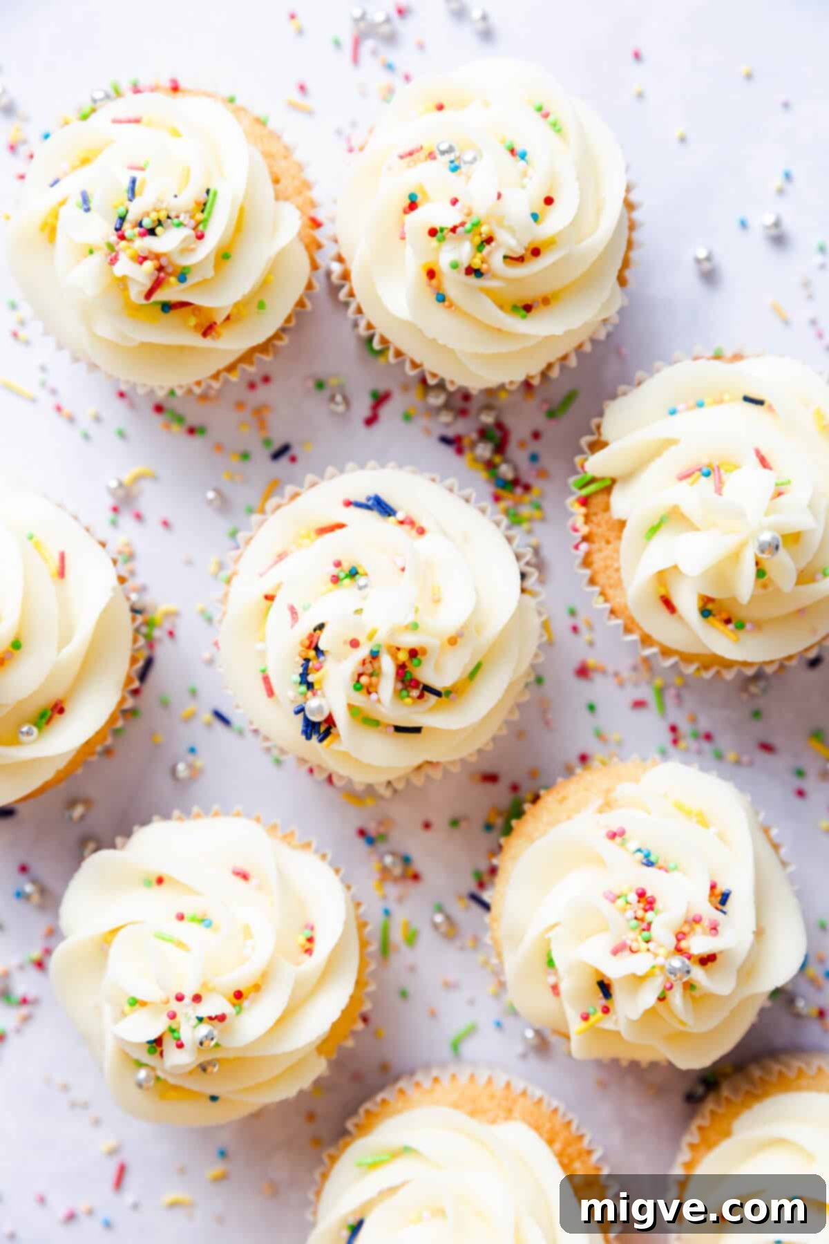 An overhead shot showcasing a delightful array of vanilla cupcakes, each adorned with creamy buttercream and a generous sprinkle of colorful decorations.