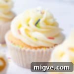 Side super close-up of a vanilla cupcake topped with buttercream and sprinkles, emphasizing its delectable appearance.