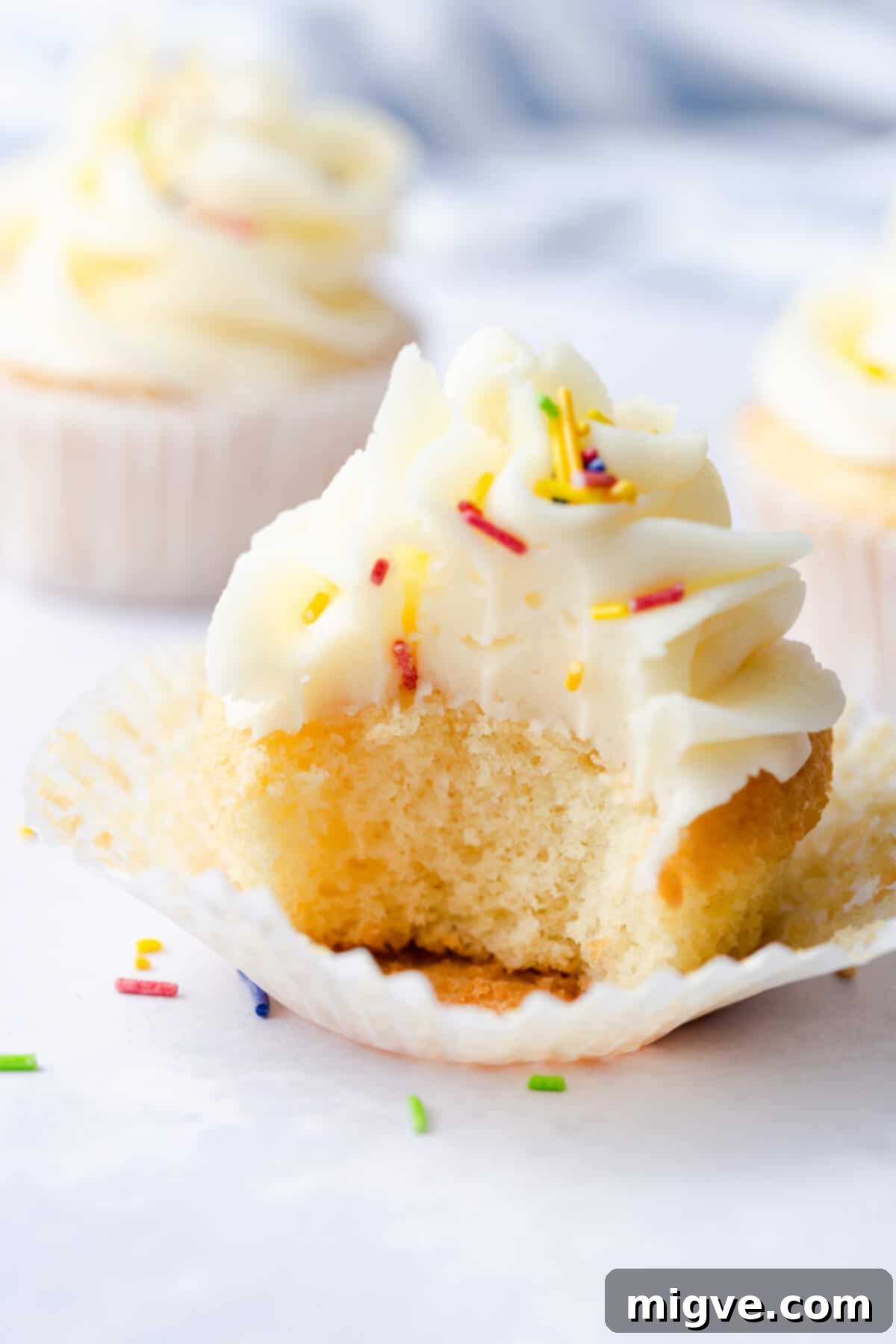 A side close-up of a perfectly baked vanilla cupcake with a bite taken out, revealing its incredibly moist and light interior, highlighting the soft crumb.