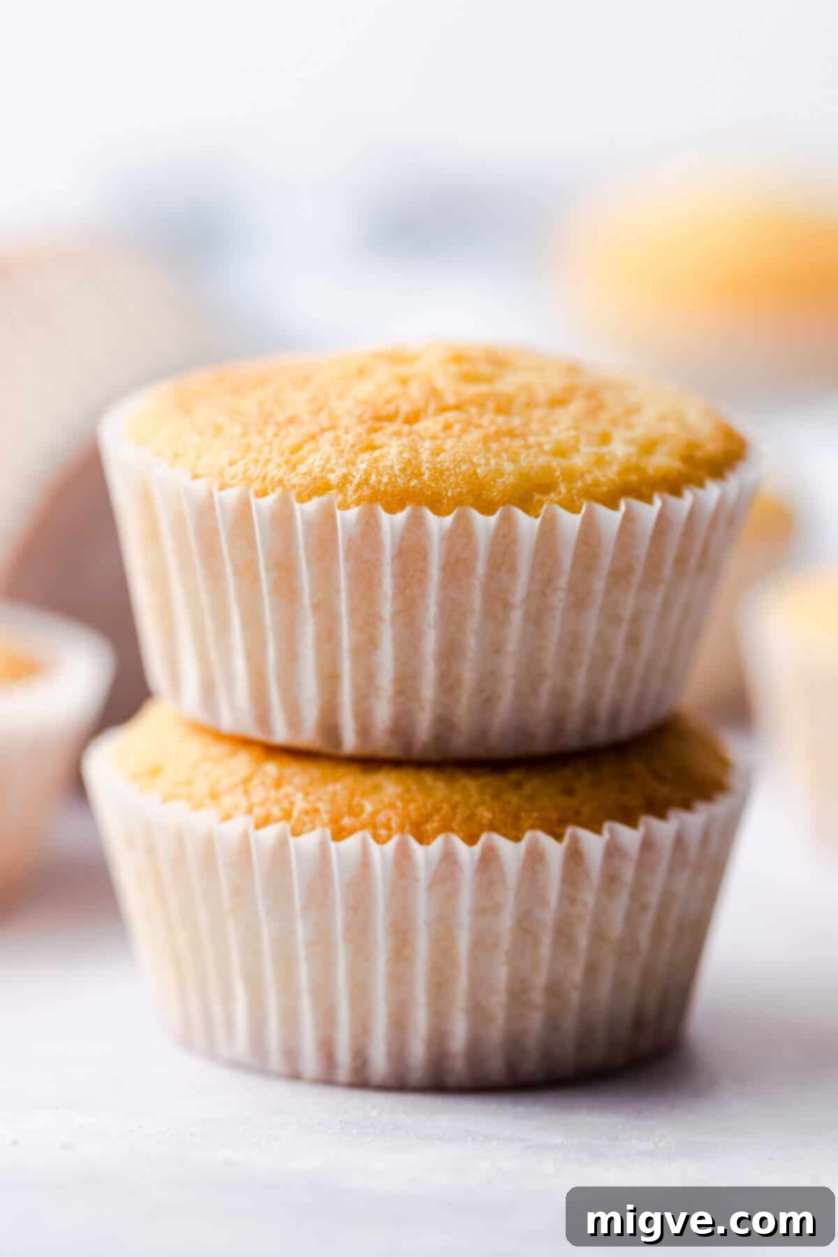 A straight-ahead super close-up view of three perfectly baked one-bowl vanilla cupcakes, stacked elegantly, highlighting their beautiful golden tops and inviting appearance.