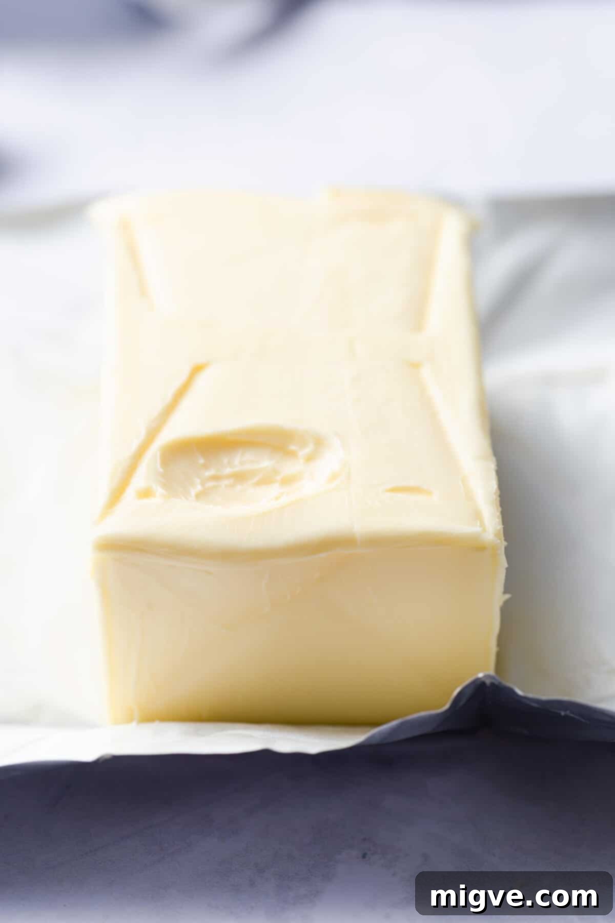 A side-angle photo of a block of softened butter exhibiting a perfect fingerprint indent, indicating it's at the optimal room temperature for baking.