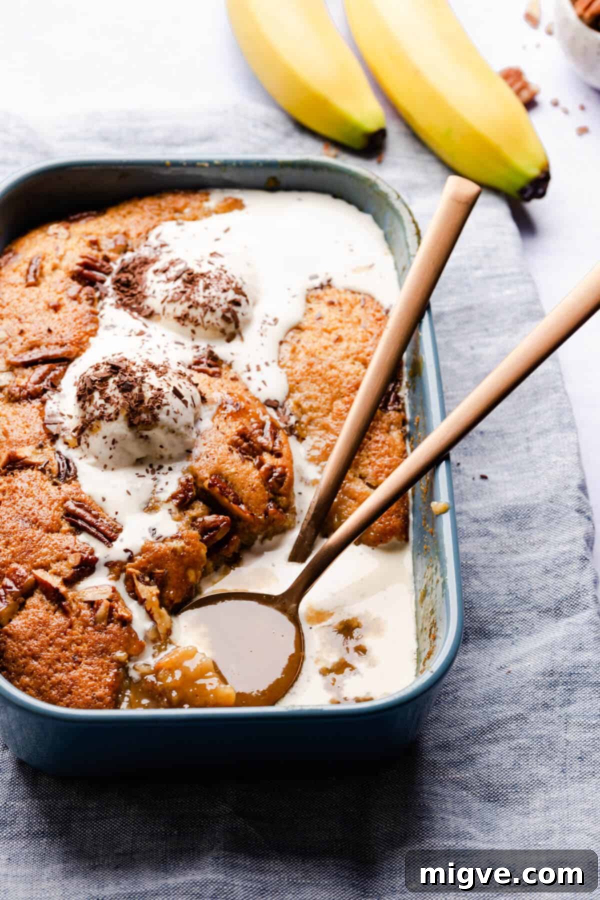 A delectable slice of self-saucing banana pudding, adorned with melting ice cream, revealing its luscious caramel sauce beneath