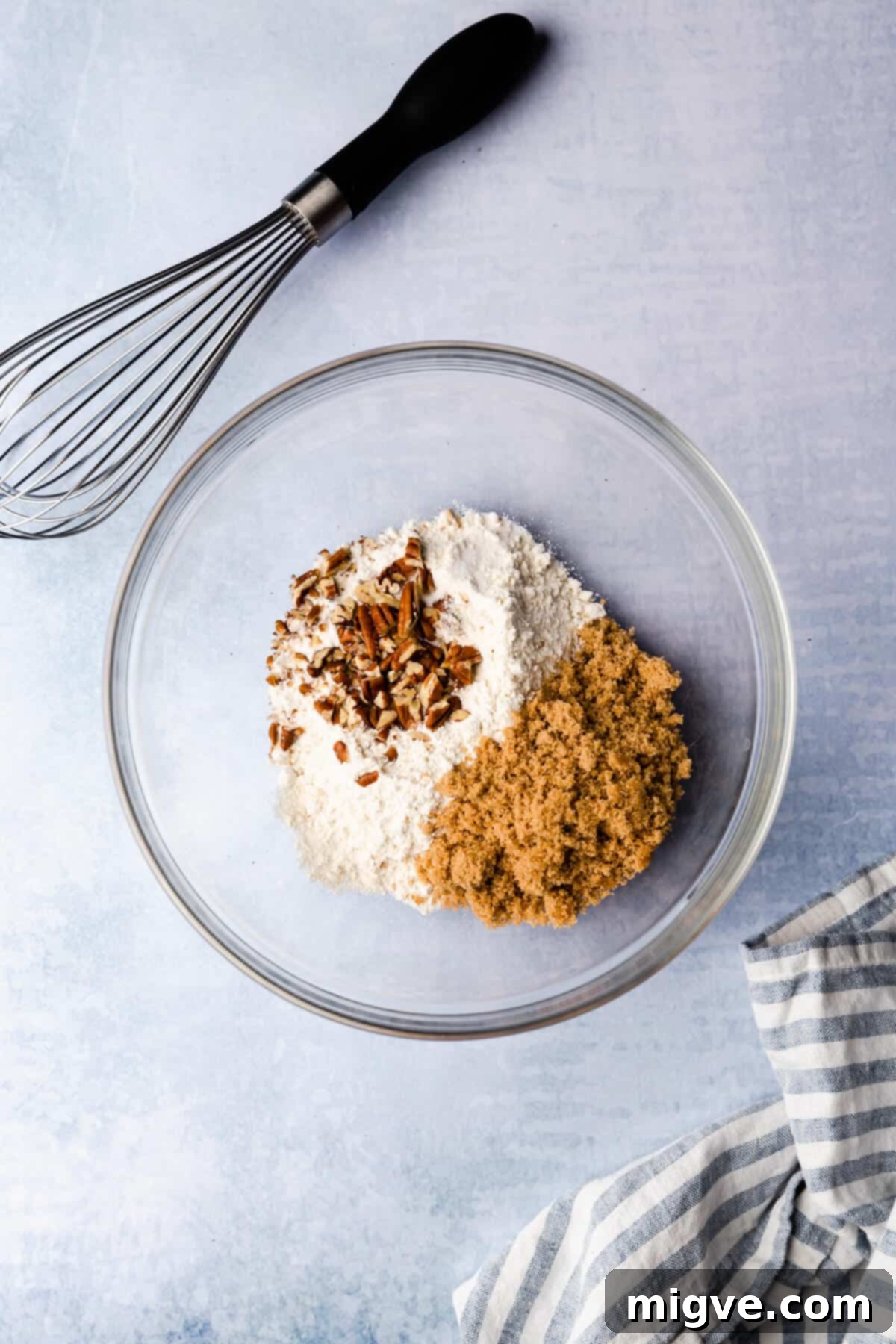Top view of a mixing bowl containing dry ingredients with a whisk resting on the side, ready for combining