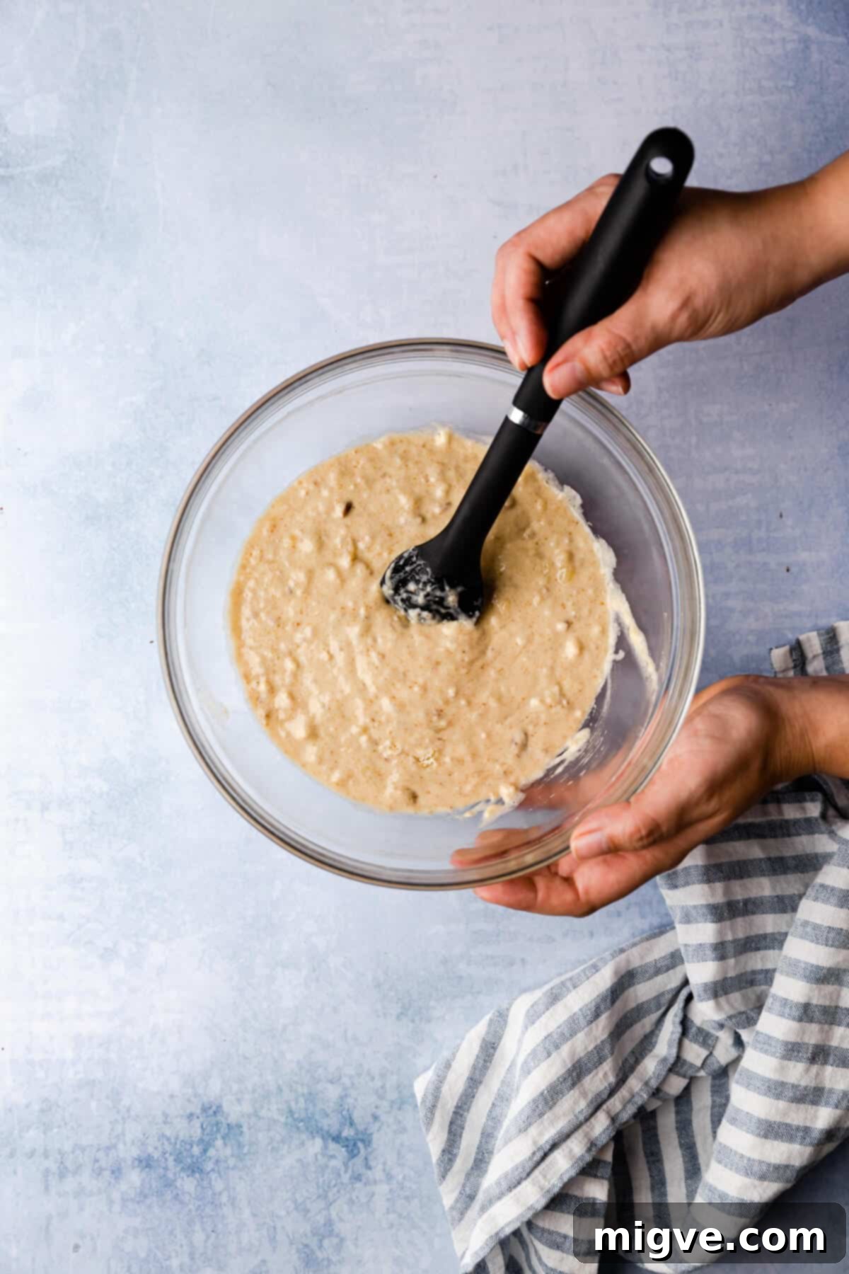Top view of a person gently mixing the pudding batter in a bowl with a spatula, ensuring a smooth consistency