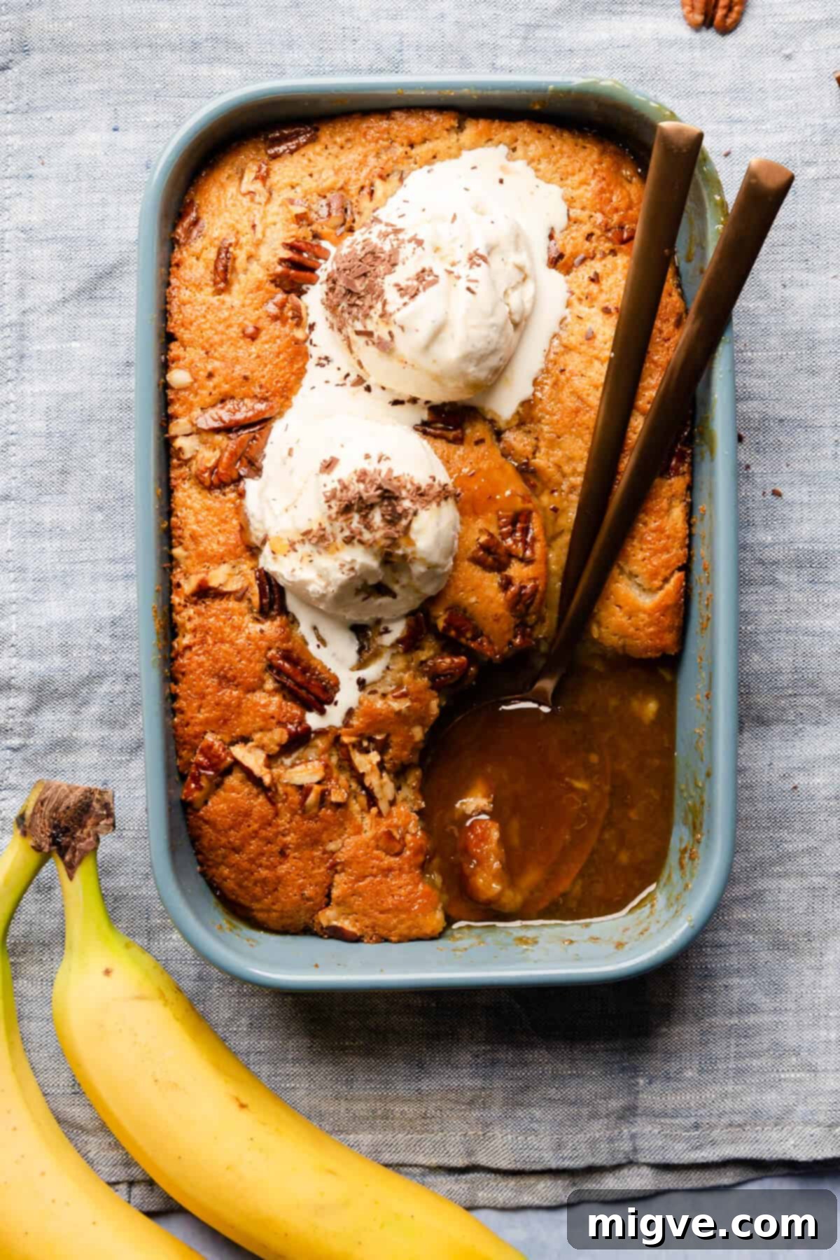 An inviting top-down view of a baking dish containing self-saucing banana pudding, generously topped with melting ice cream