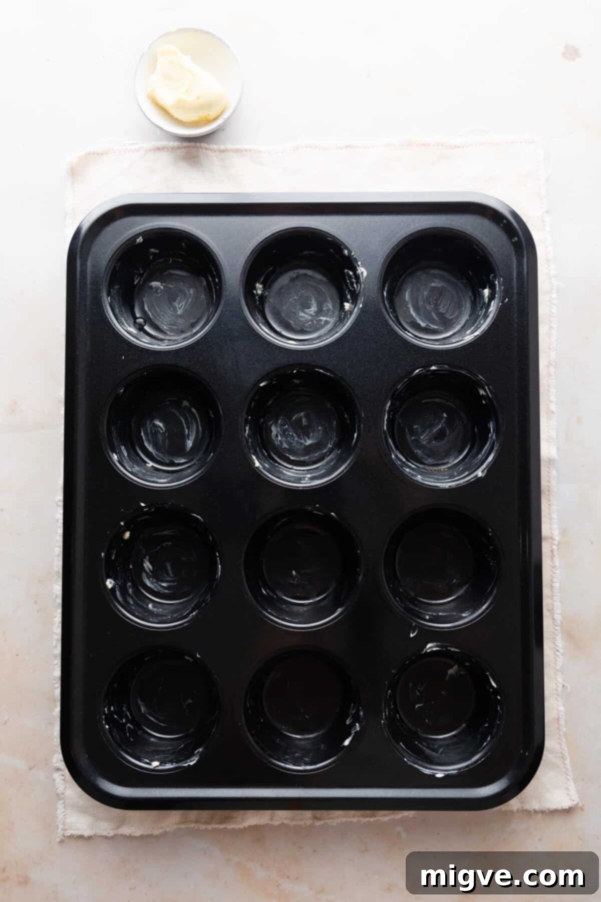 overhead view of a 12- hole muffin tin greased with butter