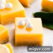 Side angle super close up at a square slice of lemon curd bars topped with mini-meringue, showcasing the layers.