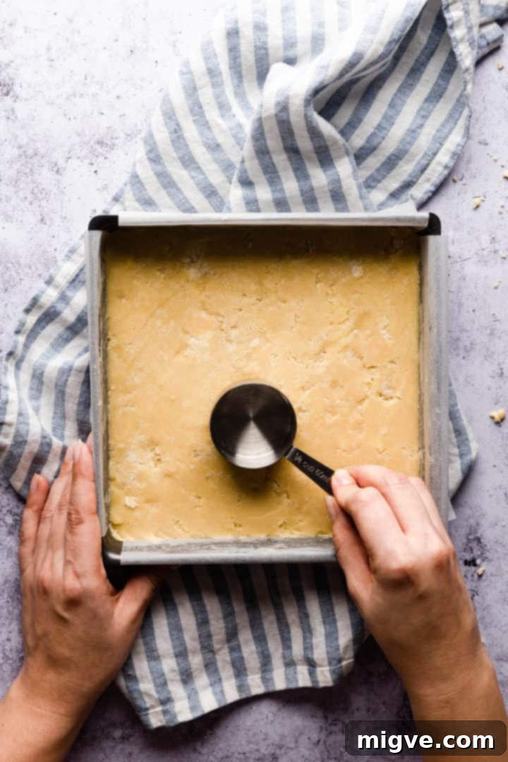 Top view of a person pressing the back of a measuring cup on shortcrust base, ensuring an even layer.