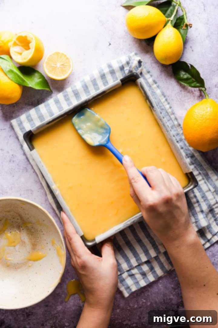 Overhead shot of a person smoothing the top of the lemon curd slices with a spatula for a perfect finish.