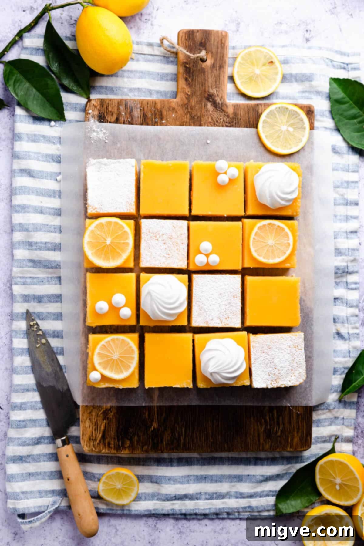 Overhead photo of 16 lemon curd slices neatly arranged on a wooden chopping board, ready to be enjoyed.