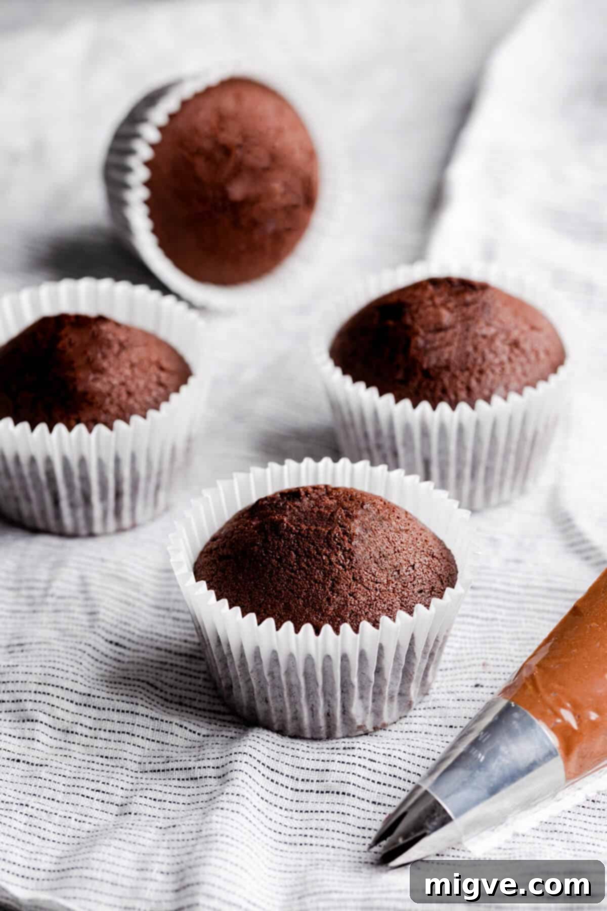 Side angle photo of 4 small batch chocolate cupcakes in their colorful paper cases, ready for frosting.