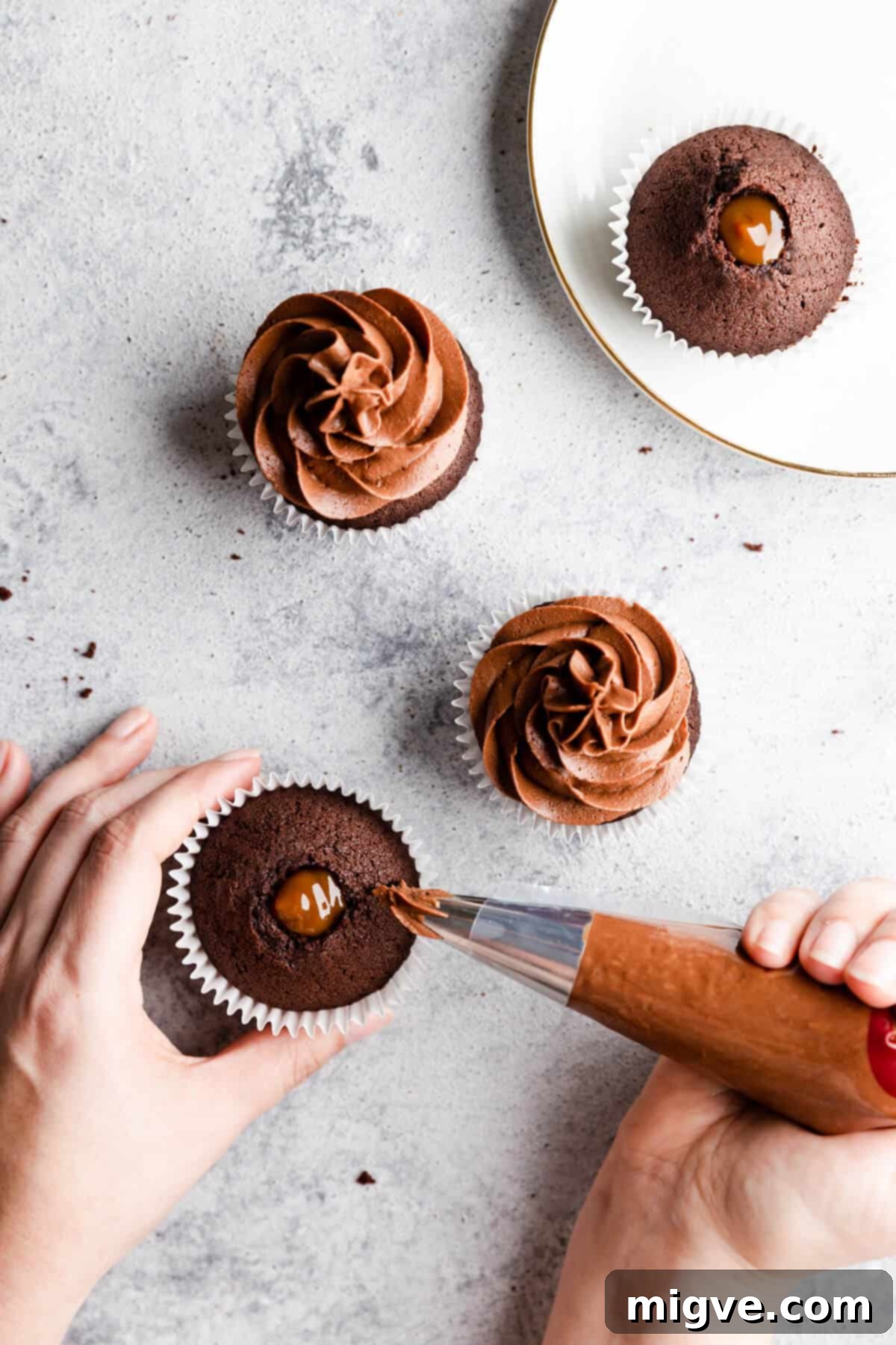 Top view of chocolate cupcakes being delicately topped with rich chocolate buttercream using a piping bag.