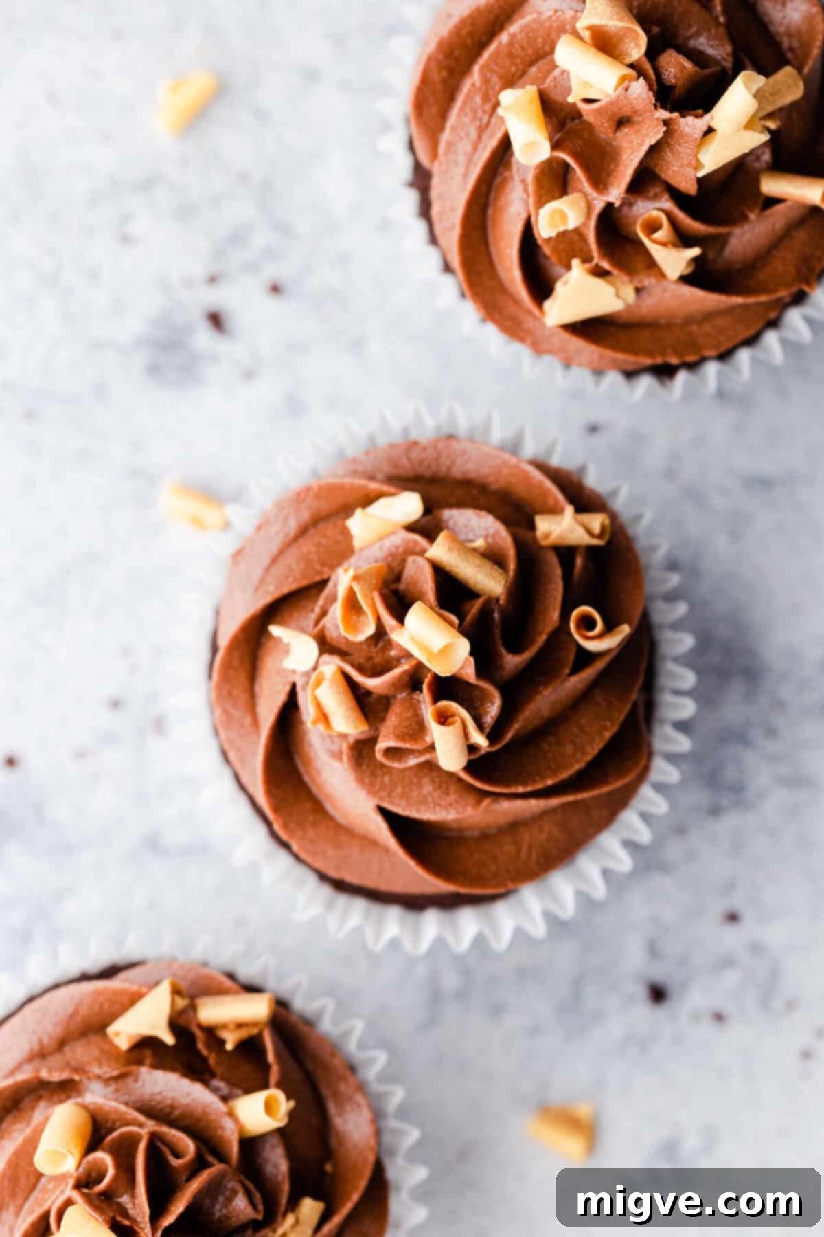 Overhead shot of 3 beautifully frosted chocolate cupcakes, adorned with smooth chocolate buttercream.