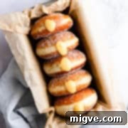 Handcrafted Doughnut Bliss 12 Top-down close-up of five small batch doughnuts, generously filled with orange curd, presented in a baking tin.