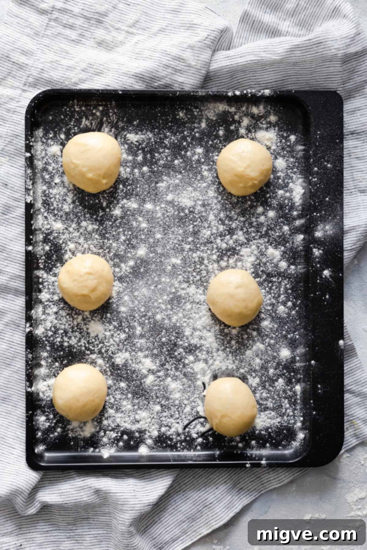 Handcrafted Doughnut Bliss 6 Top-down view of six perfectly portioned dough balls for small batch doughnuts, neatly arranged on a lightly floured baking tray, poised for their second prove.