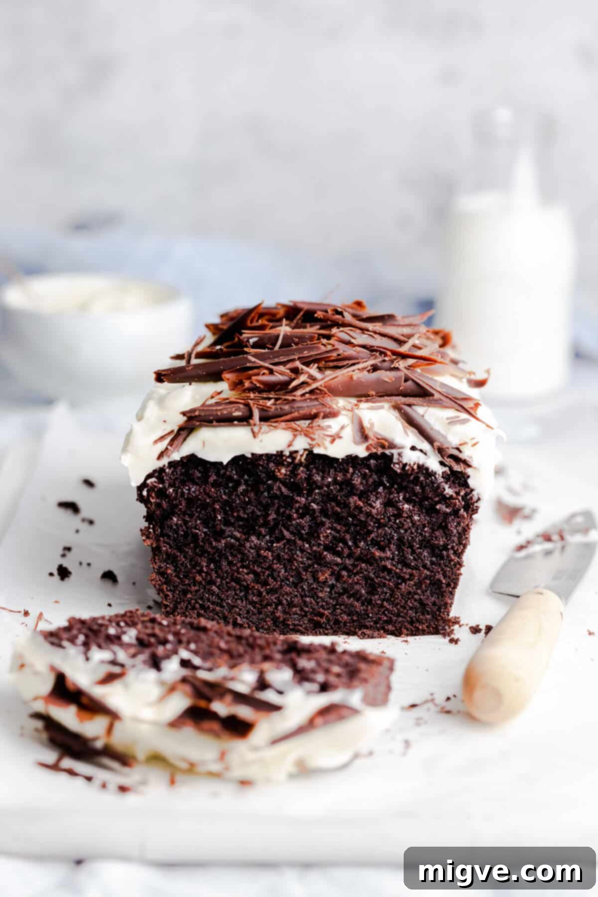 45 degree angle photo of chocolate loaf cake with frosting and with slice cut of