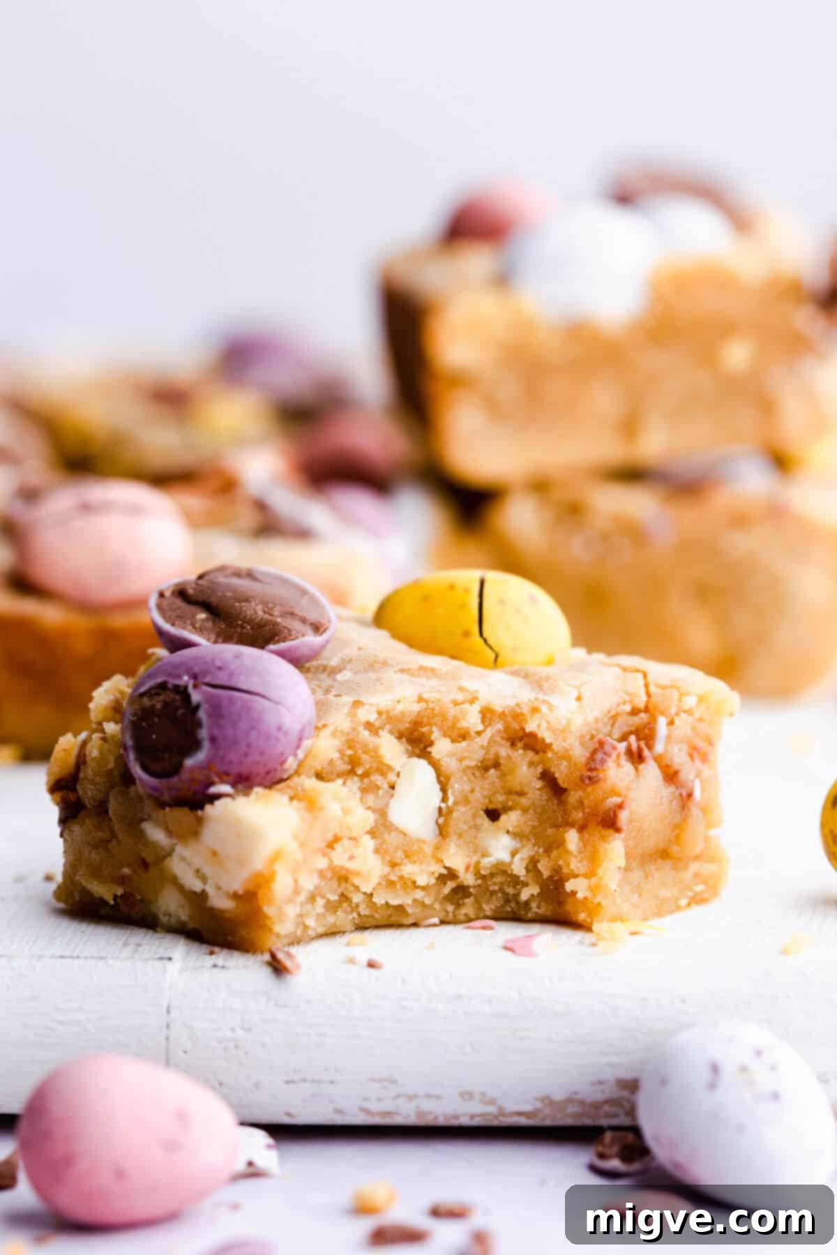 Speckled Spring Blondies 9 Side angle super close-up of a mini egg blondie bar with a bite taken out, showing its gooey interior.