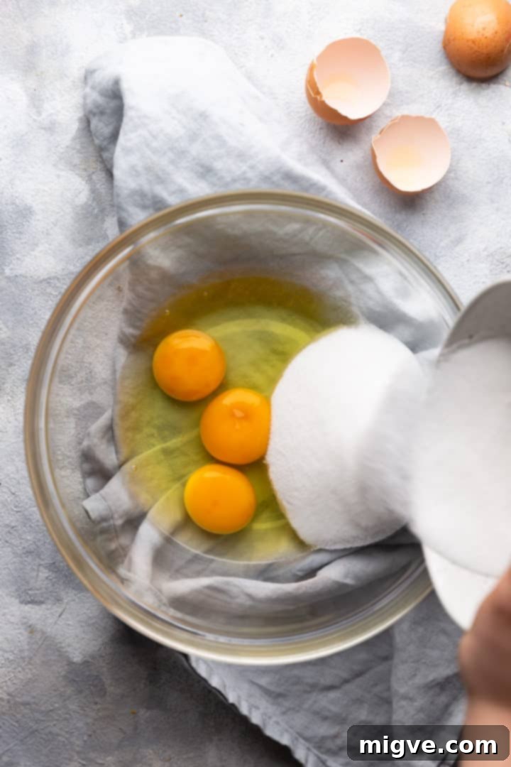 top view of sugar being added to bowl with eggs