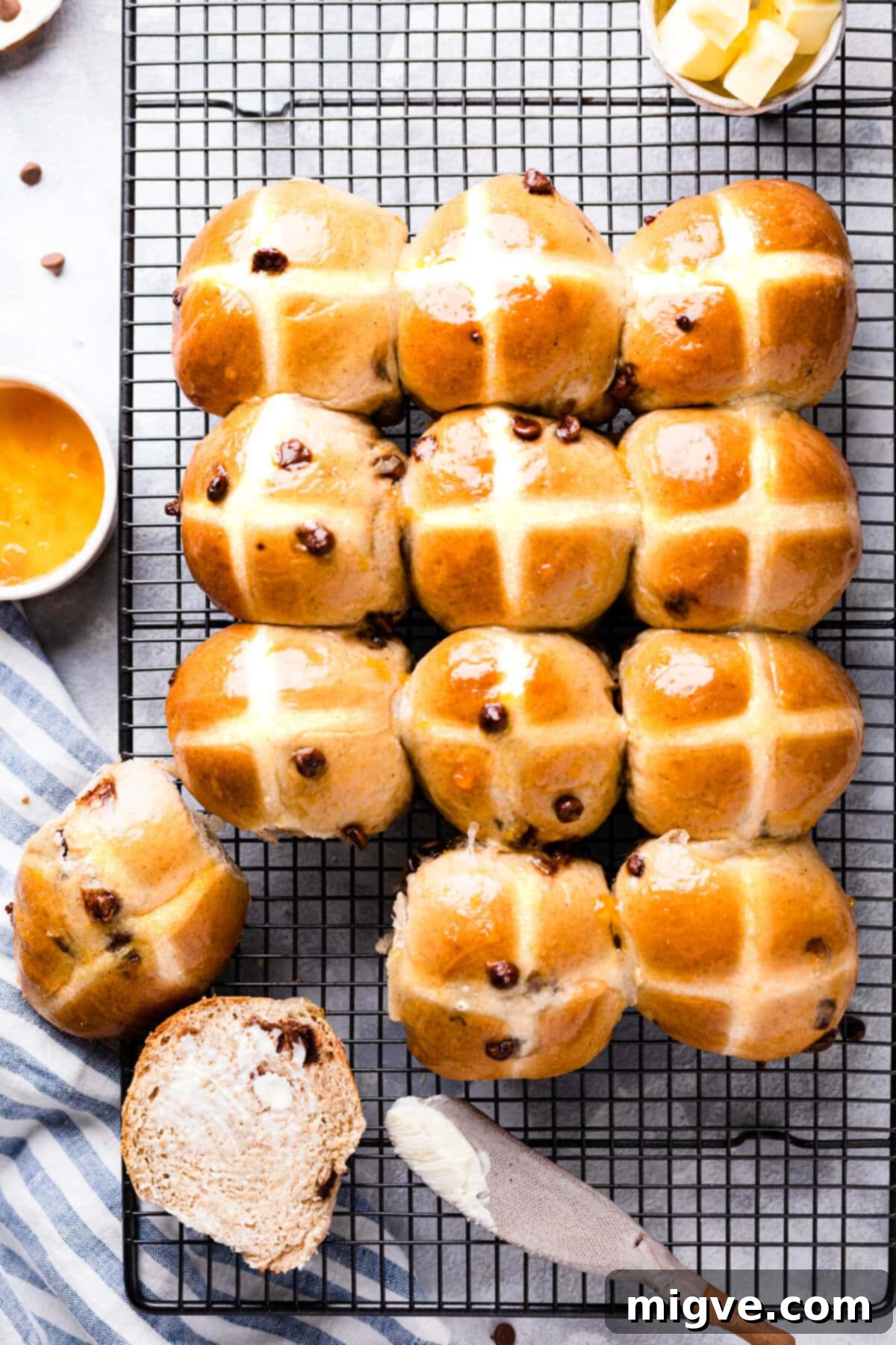An overhead view of freshly baked, shiny chocolate chip hot cross buns arranged neatly on a wire cooling rack, highlighting their perfect golden-brown crusts and distinct crosses.