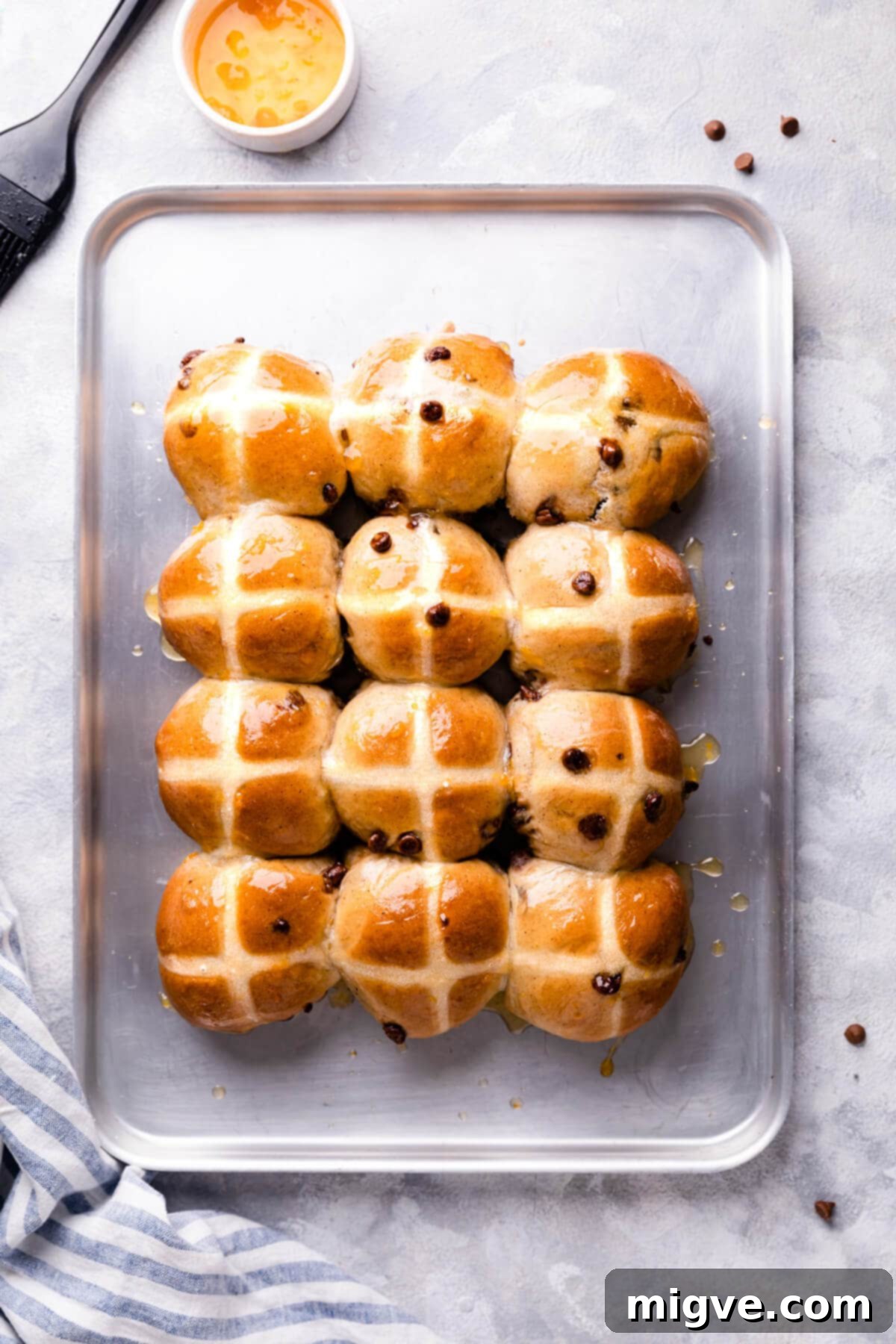 A top-down shot of a baking sheet filled with freshly baked chocolate chip hot cross buns, showcasing their golden-brown tops and distinct white crosses.