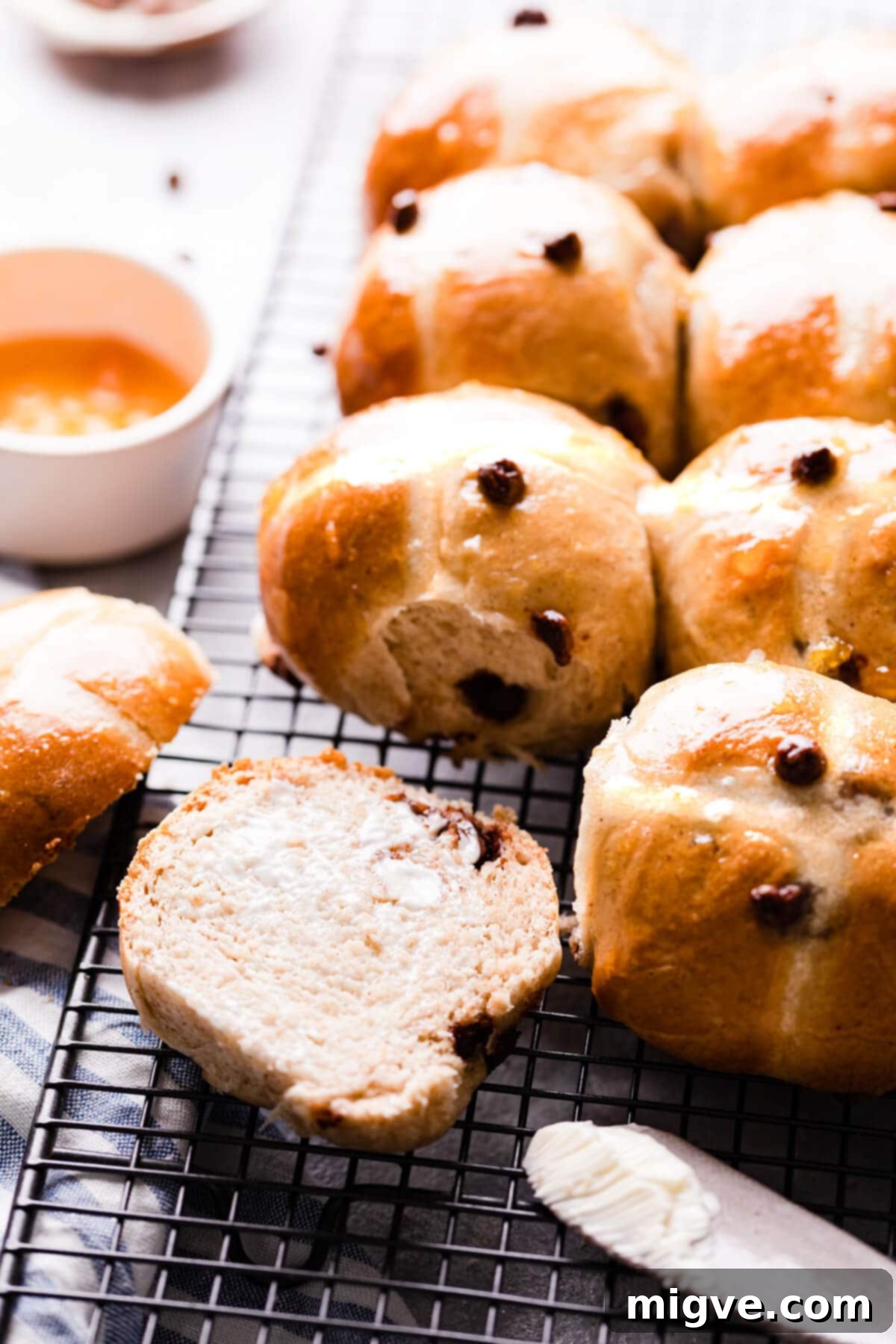 A close-up side angle photo showing a chocolate chip hot cross bun sliced in half, revealing its fluffy interior, melted chocolate chunks, and a hint of marzipan.