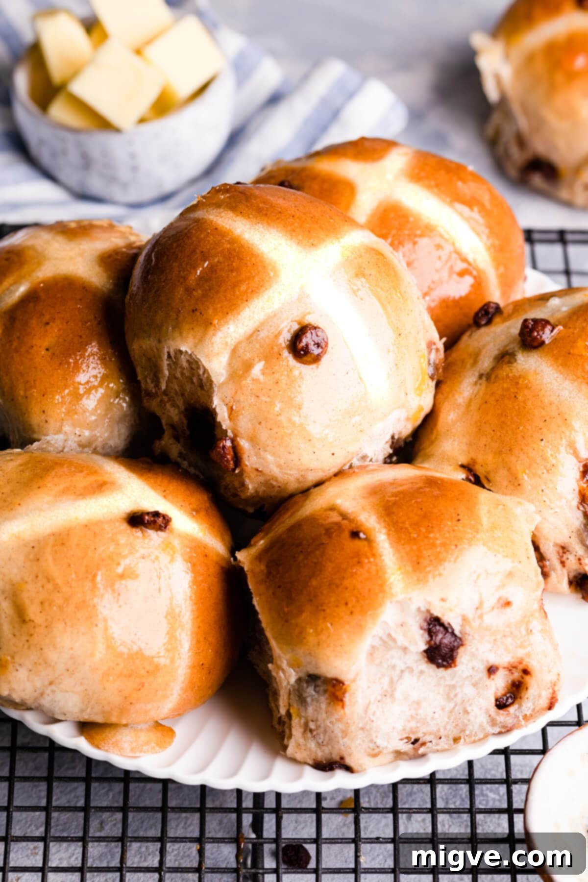 A side view of golden-brown chocolate chip hot cross buns artfully arranged on a white plate, showcasing their fluffy texture and glaze.