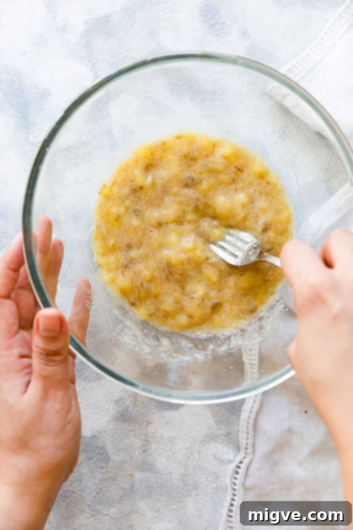 A person mashing ripe bananas in a bowl, a crucial step for achieving moist and flavorful banana blueberry muffins.