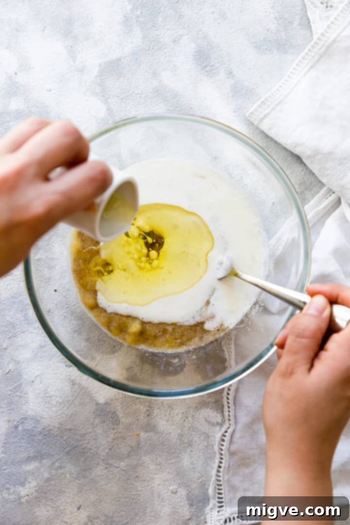Olive oil being poured into a bowl with other wet ingredients, adding richness and moisture to the banana blueberry muffin batter.