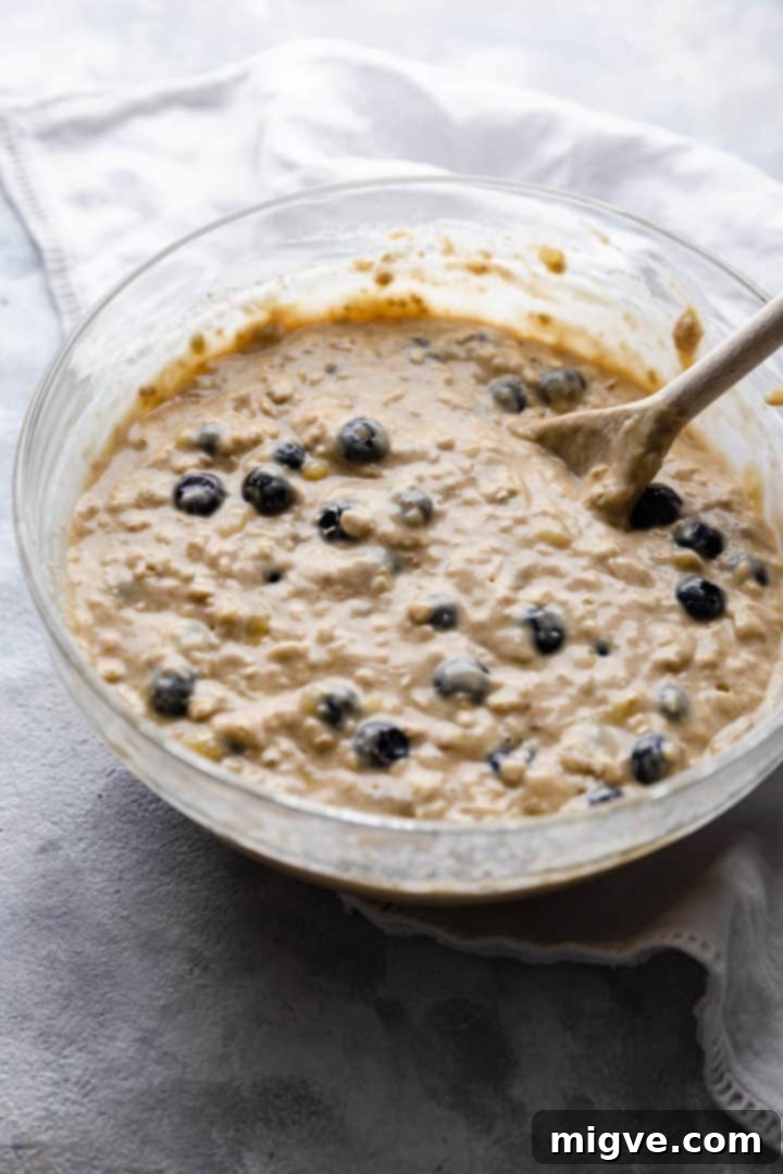Side view of a bowl filled with raw muffin batter, flecked with blueberries, ready to be scooped into the muffin tin.