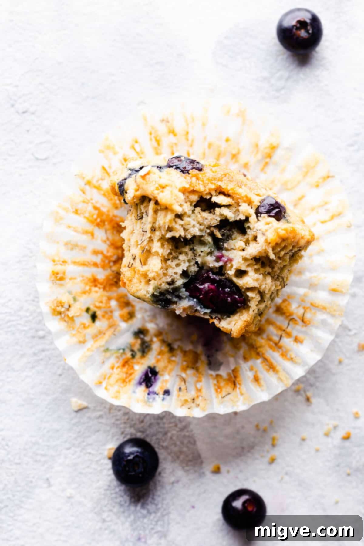 Close-up of a single banana and blueberry muffin, freshly baked and nestled in its paper case, highlighting the juicy blueberries and crunchy oat topping.