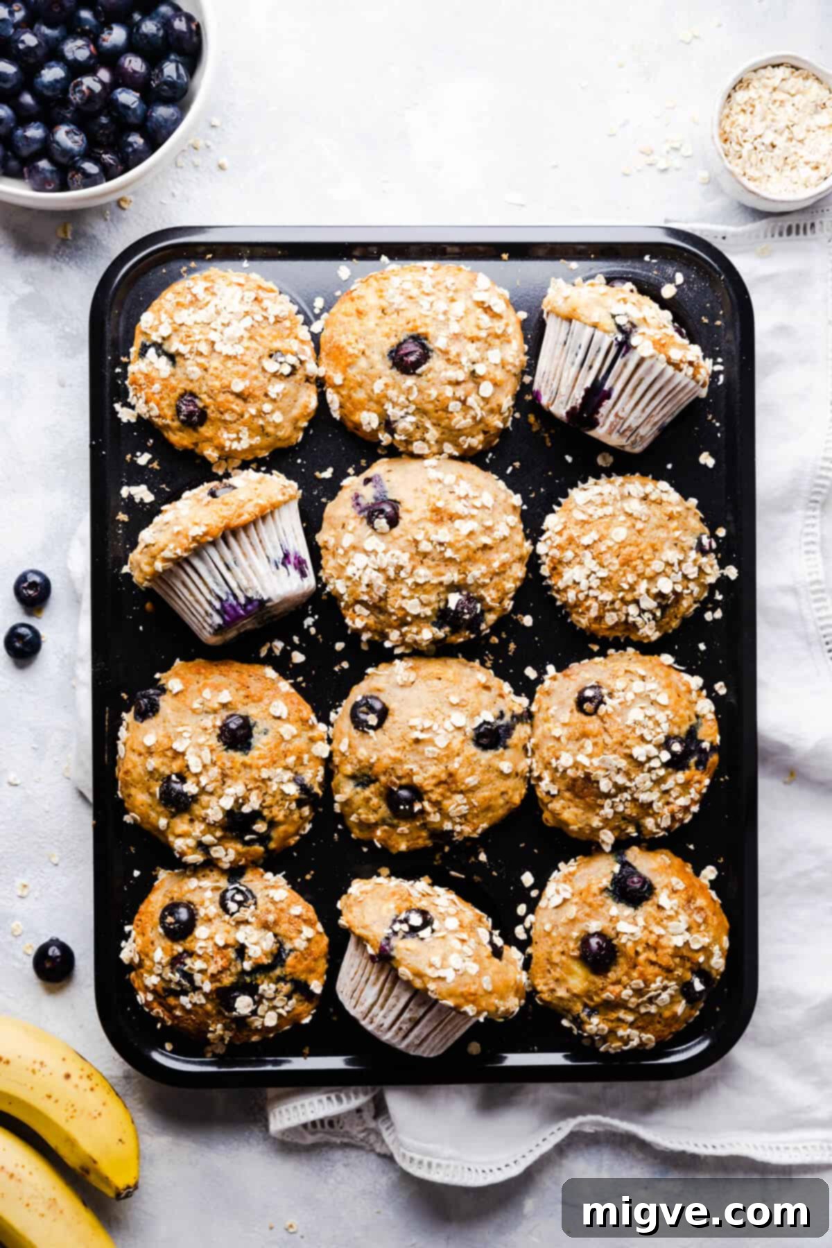 Top-down view of a muffin tin generously filled with golden-brown banana and blueberry muffins, fresh from the oven and cooling.