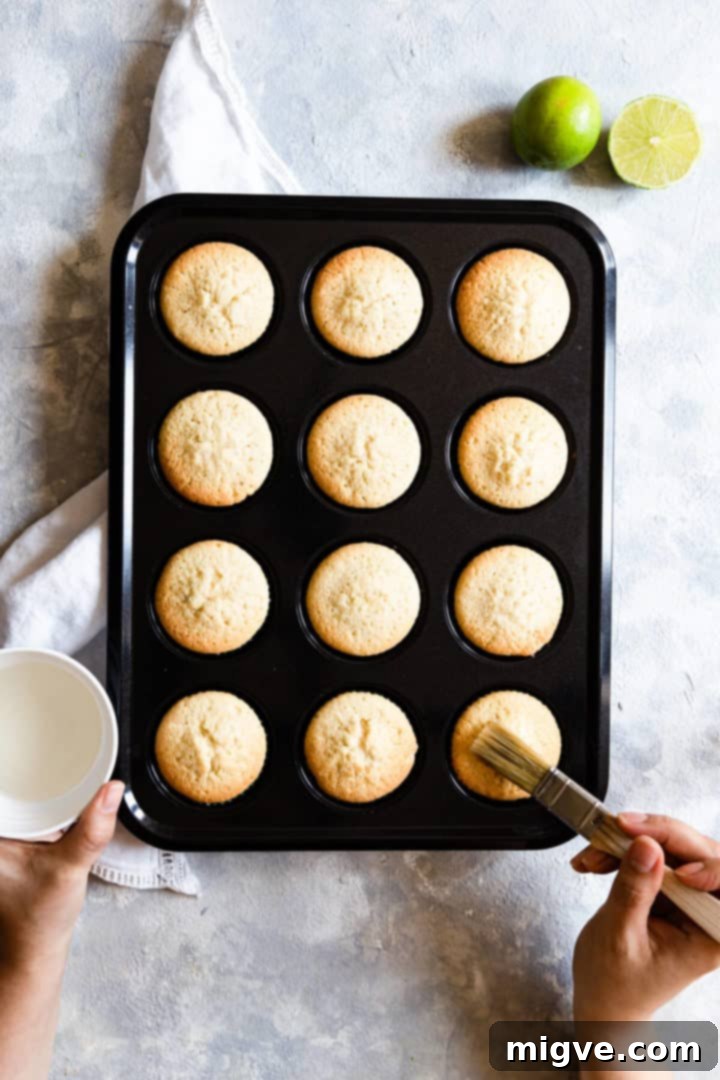 Overhead shot of a person carefully brushing warm cupcakes with the prepared gin and tonic syrup.