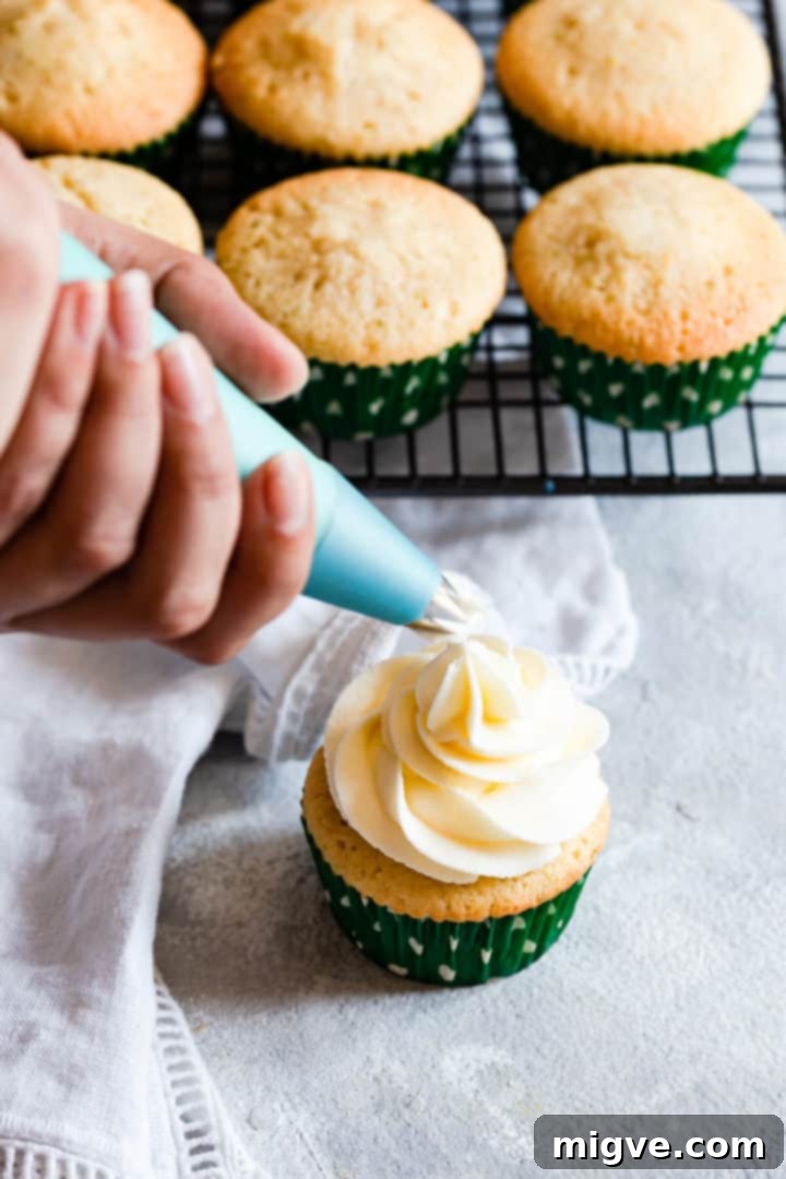 Side close-up of a beautiful swirl of butter icing being piped onto the top of a cooled cupcake.