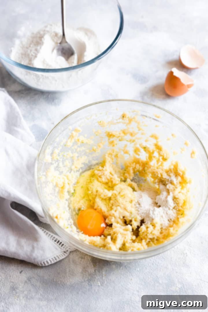 Top view of a bowl containing whipped butter, an egg, and a spoonful of flour, midway through the mixing process.
