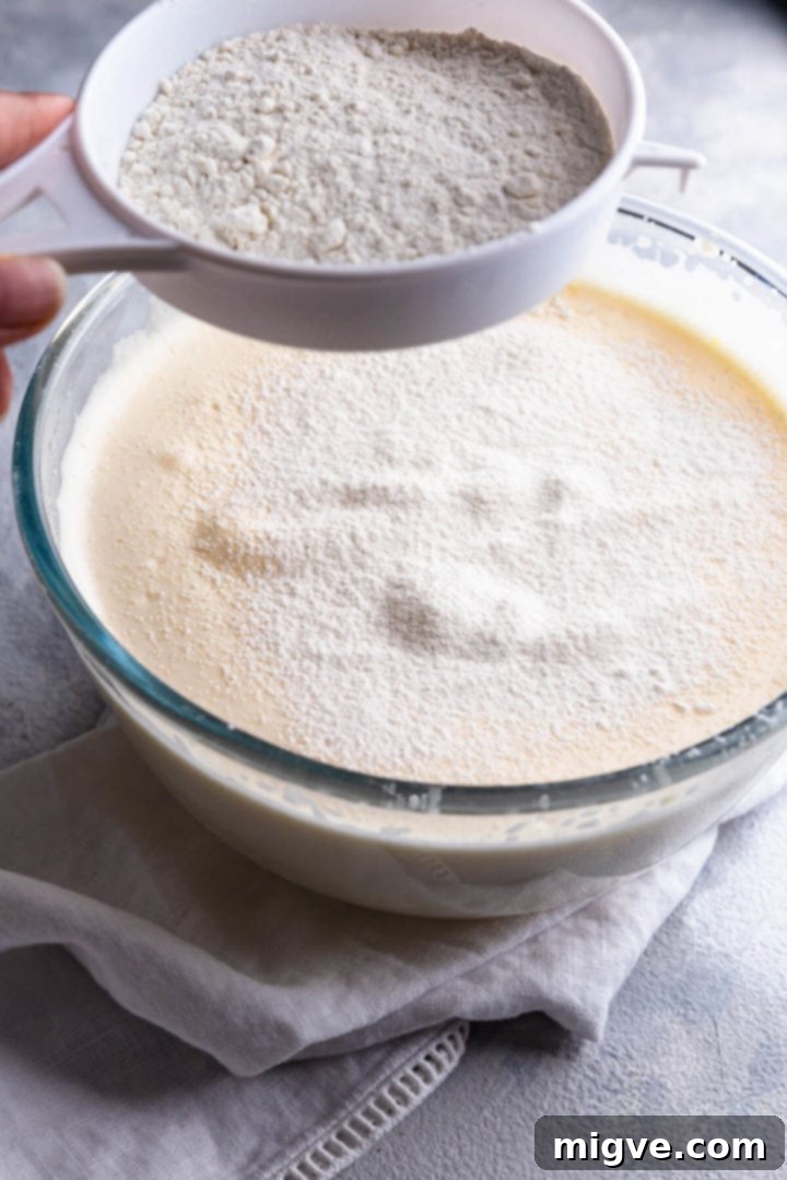 side view of a cake batter in a bowl with flour being sieved on top