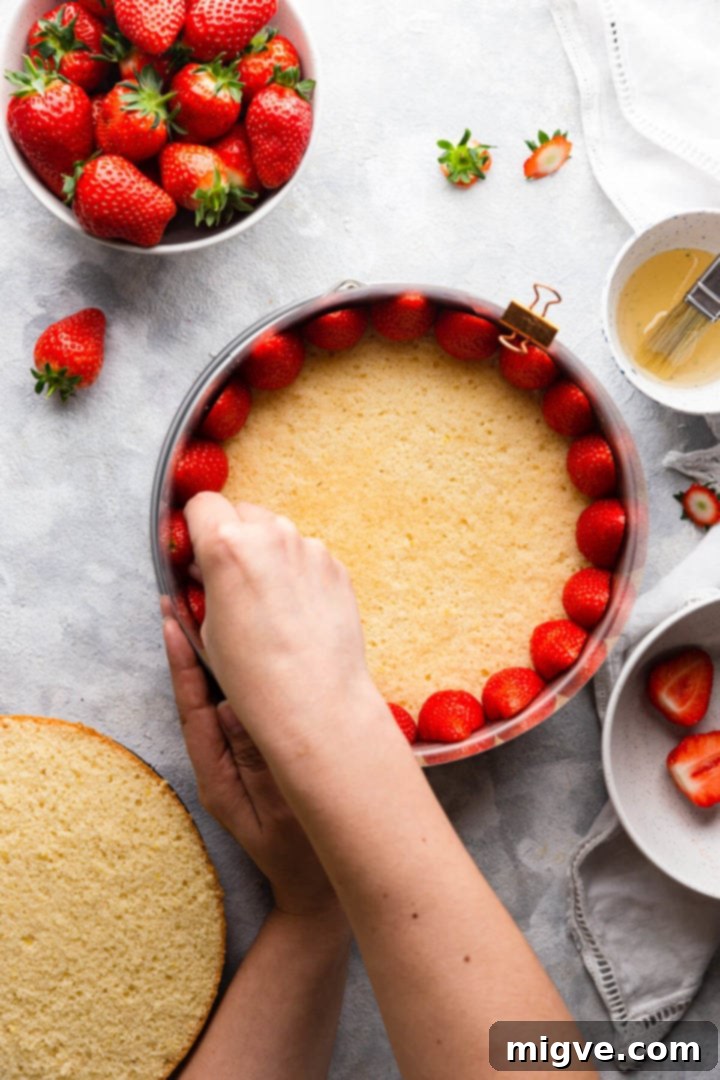 overhead shot of a person fitting fresh strawberries inside of the baking tin