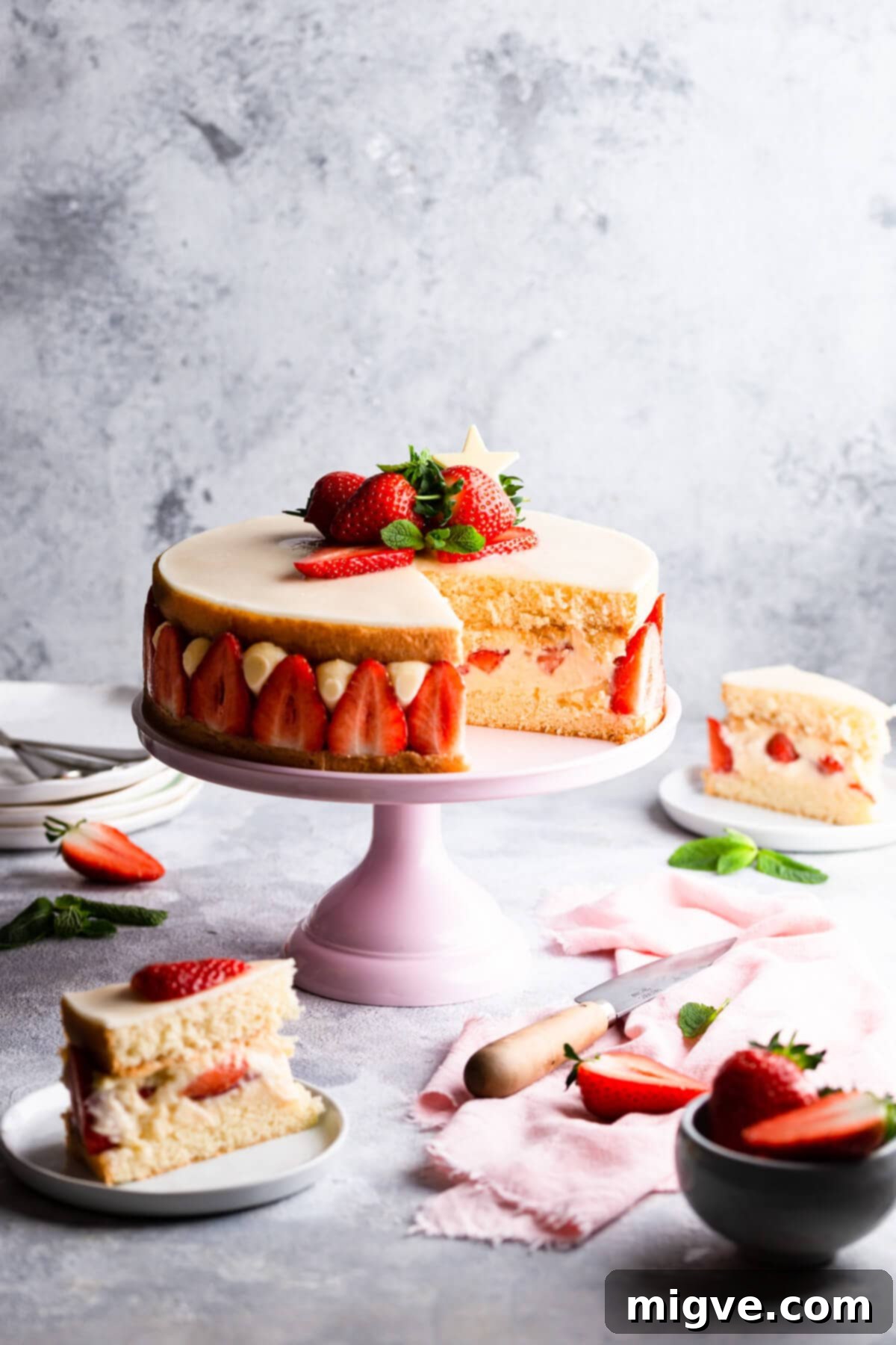 side view of strawberry cake on pink cake stand with couple of slices cut out