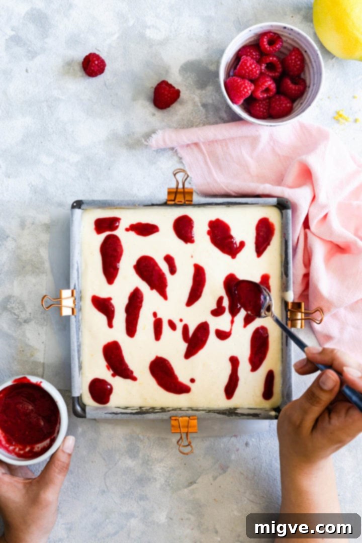 Lemon Raspberry Cheesecake Delights 10 Overhead view of a person artfully adding dollops of raspberry sauce onto the creamy cheesecake batter
