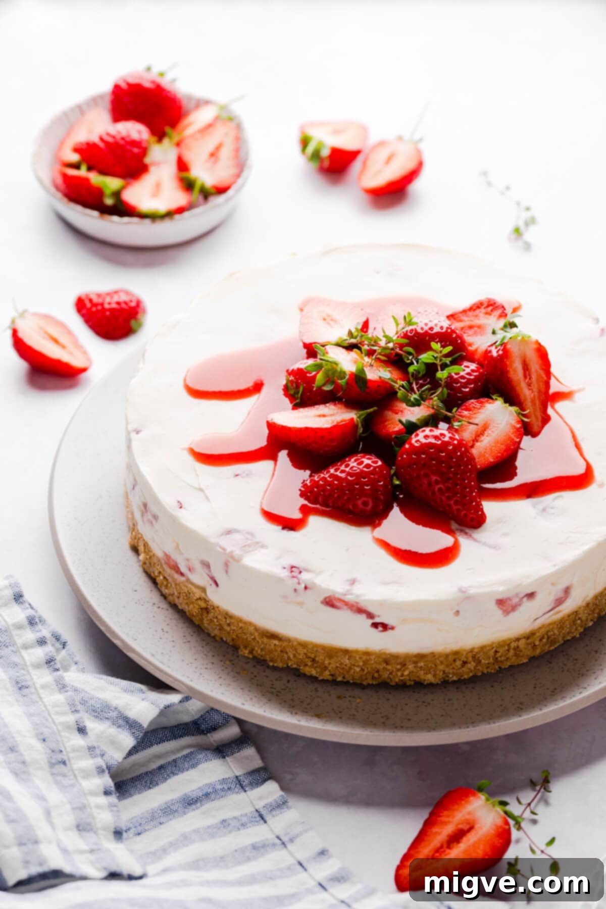 Velvet Strawberry White Chocolate Cheesecake 2 side angle view of strawberry white chocolate cheesecake topped with fresh strawberries and sauce