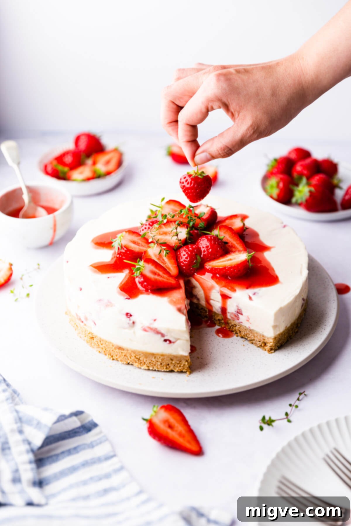 Velvet Strawberry White Chocolate Cheesecake 13 side angle of strawberry cheesecake being topped with fresh strawberry