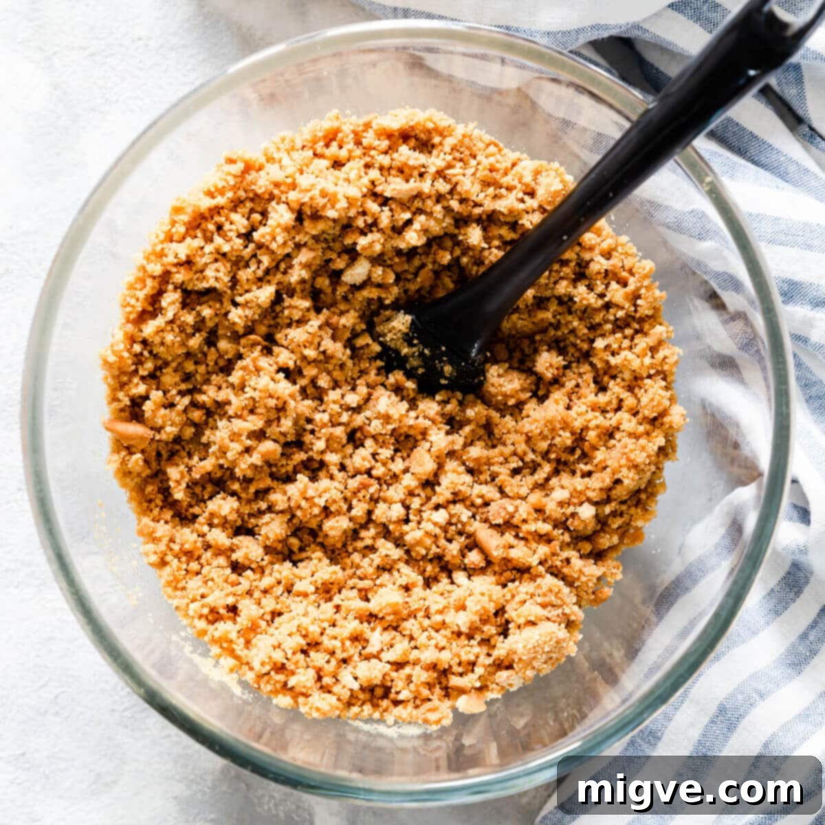 Velvet Strawberry White Chocolate Cheesecake 5 overhead shot of a bowl with a mixture of crushed biscuits and melted butter