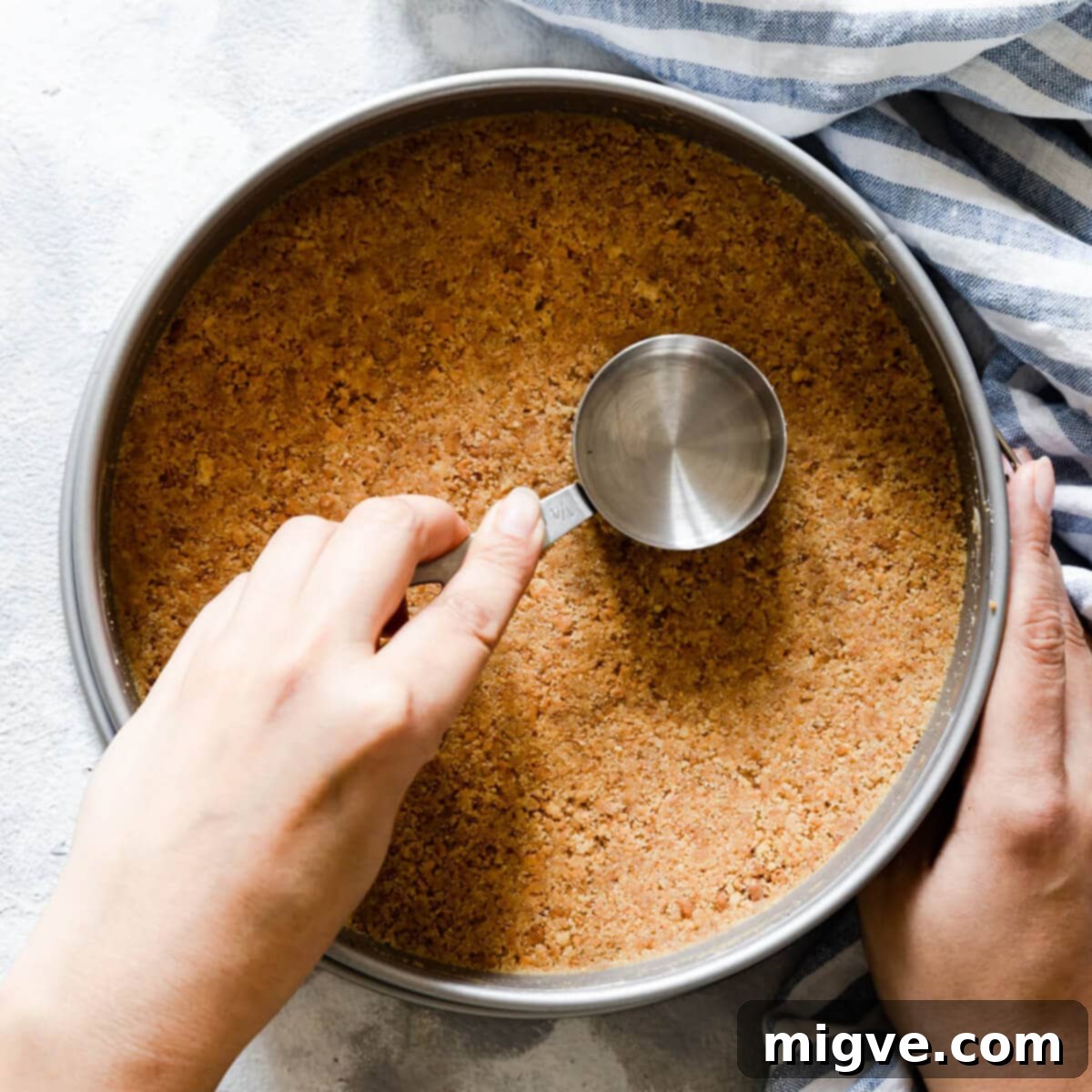 Velvet Strawberry White Chocolate Cheesecake 6 top view of a person pressing biscuit base into cake tin